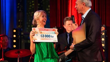 Jennifer McShane håller i en check och ler mot Postkodlotteriets ena Managing Director