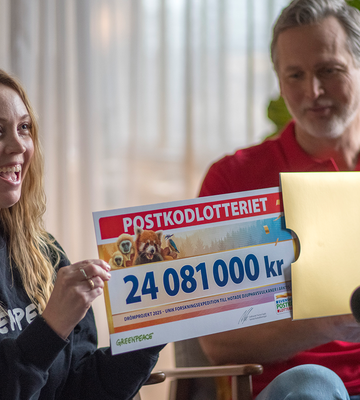 Kvinna drar ut en check från Postkodlotteriet från ett guldkuvert