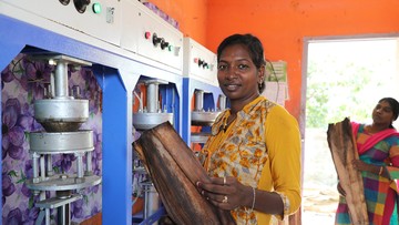 Kvinna med vedträ framför en maskin.