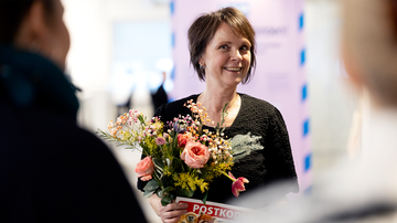 Kvinna håller i en bukett blommor och en check från Postkodlotteriet