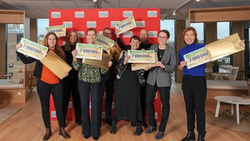 Personer håller upp checkar från Postkodlotteriet